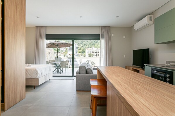 A modern hotel room with a bed, a sofa, a dining area, and a TV.