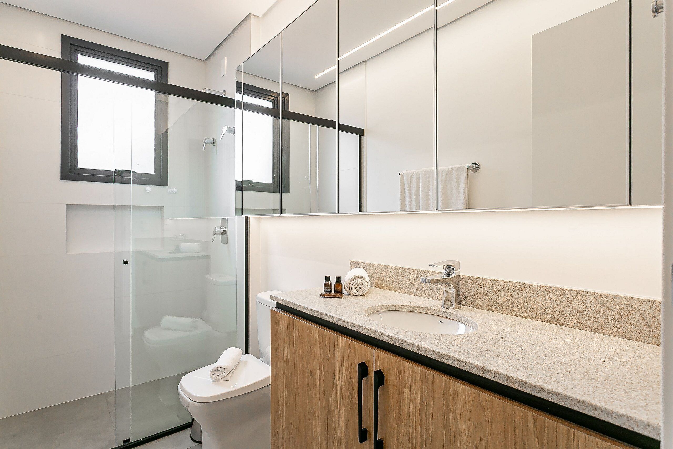 Een moderne badkamer met een douchecabine van glas, een toilet, een wastafel met spiegel erboven, en houten kastjes.