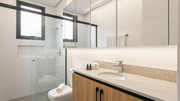 Een moderne badkamer met een douchecabine van glas, een toilet, een wastafel met spiegel erboven, en houten kastjes.