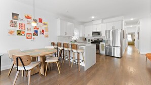 A modern kitchen with white cabinets, stainless steel appliances, and a wooden dining area.