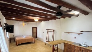 A room with a bed, a desk, a chair, a ceiling fan, and a window. - Marvin Suites (Isla Holbox)