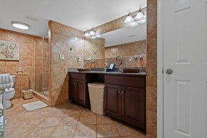 A bathroom with a glass shower enclosure, a sink with a mirror, and a toilet. - Sunset Bay Views! 3 bed, 2 bath End Unit Condo with Pool, Dock and Water Access (Pensacola Beach)
