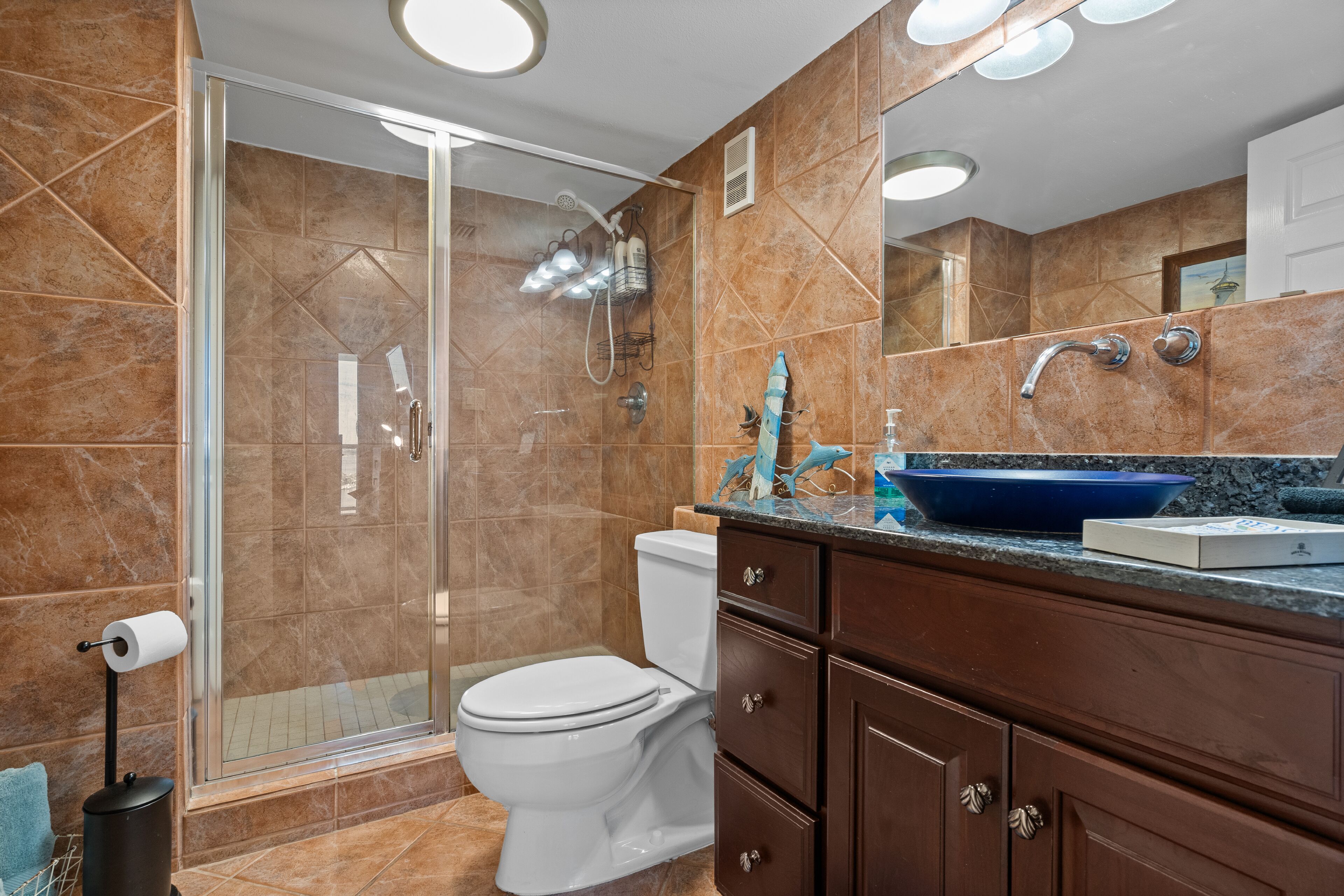 A modern bathroom with a glass-enclosed shower, a white toilet, and a dark wooden vanity with a blue sink.