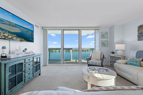 A spacious living room with a large sliding glass door leading to a balcony with a view of a body of water. - Sunset Bay Views! 3 bed, 2 bath End Unit Condo with Pool, Dock and Water Access (Pensacola Beach)