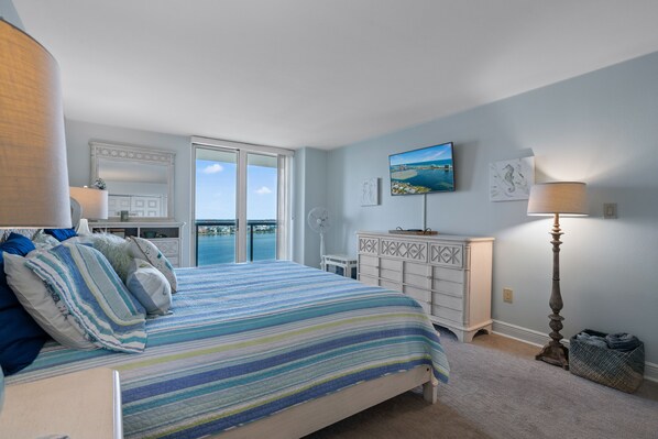 A bedroom with a bed, a dresser, a lamp, and a view of the ocean.