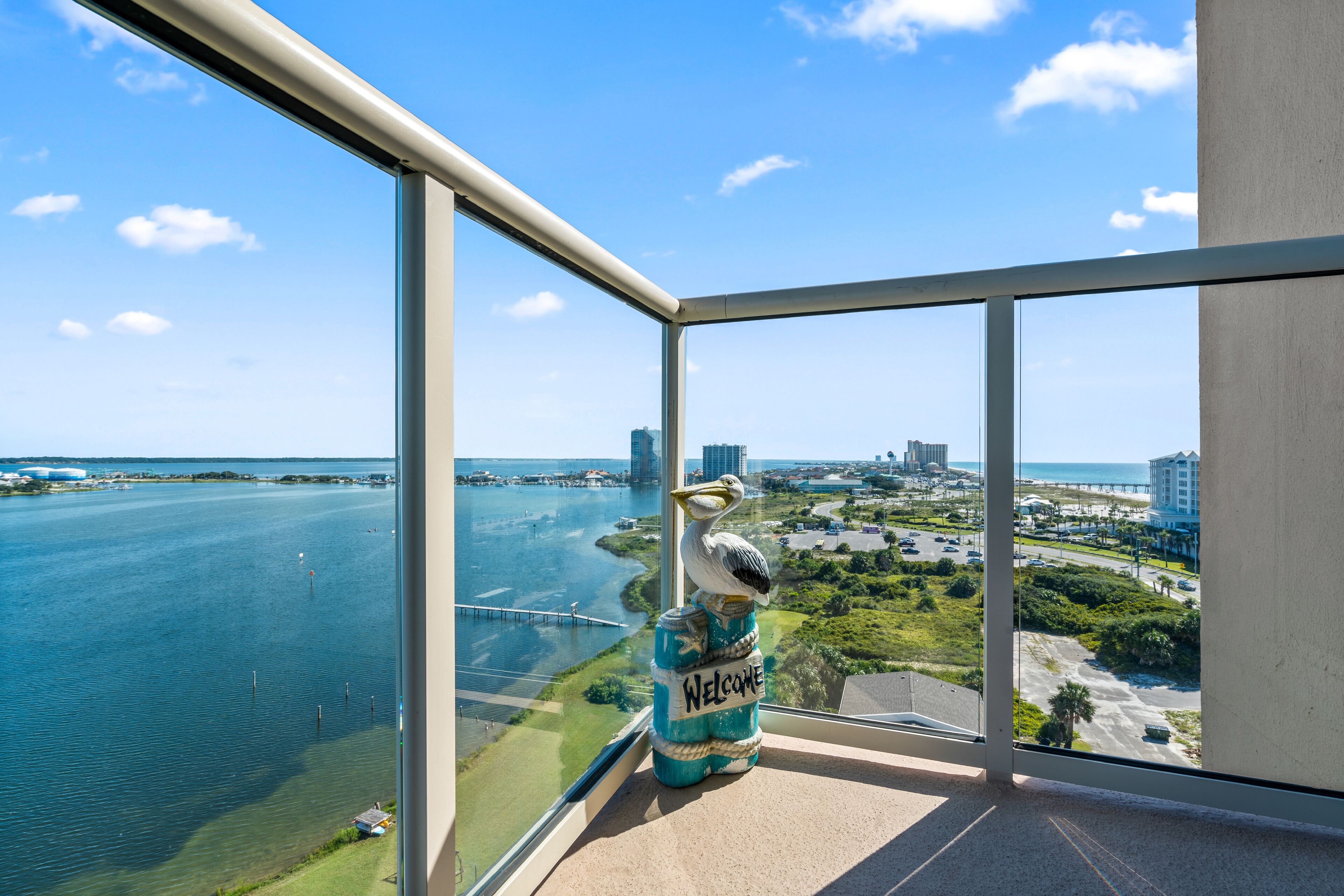 A balcony with a clear view of a waterfront, a seagull sculpture, and a 'Welcome' sign on a jar.