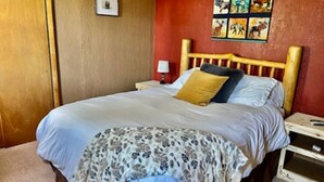 Une chambre à coucher avec une tête de lit en bois, un lit recouvert d’une couverture à motifs, une table de chevet avec une lampe et un mur orné d’œuvres d’art sur le thème des animaux.