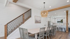 A modern kitchen with white cabinetry, a wooden staircase, and a dining area with a light-colored table and chairs.