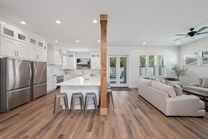 A modern kitchen with stainless steel appliances, a central island with stools, and a wooden column.