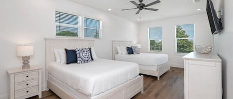 A bedroom with two beds, a ceiling fan, a TV, and a nightstand with drawers.