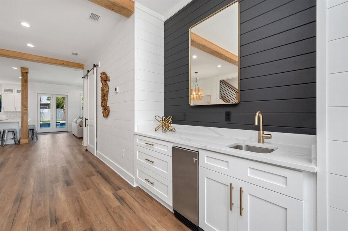 A modern kitchen with white cabinetry, a black backsplash, and a large mirror above the sink.