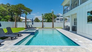 A rectangular swimming pool with a clear blue water surface, surrounded by a paved deck with lounge chairs.