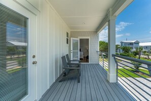 A covered porch with a wooden floor, a pair of Adirondack chairs, and a view of a residential area.