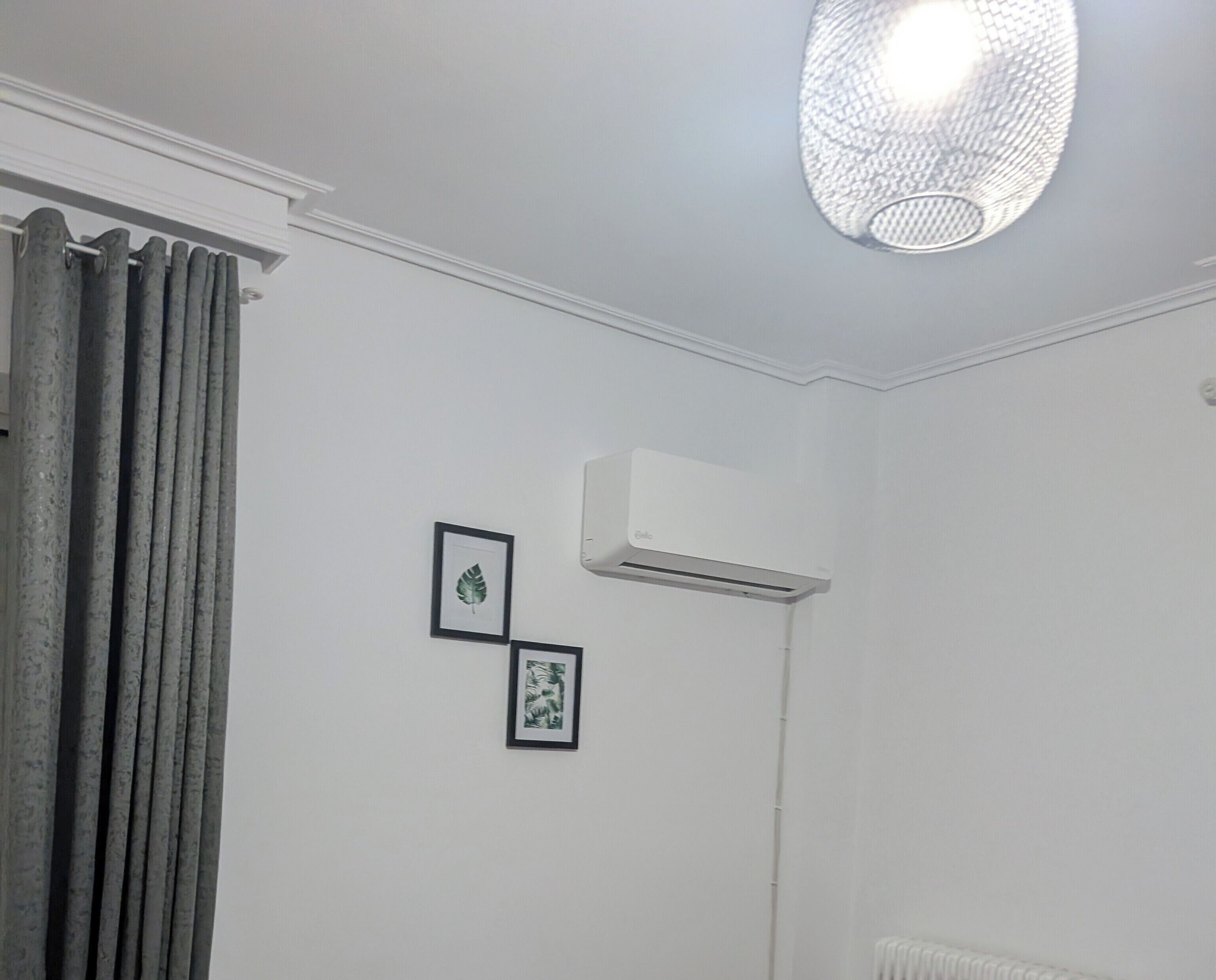 Una habitación con techo blanco, una lámpara en el techo, un equipo de aire acondicionado y dos cuadros en la pared.