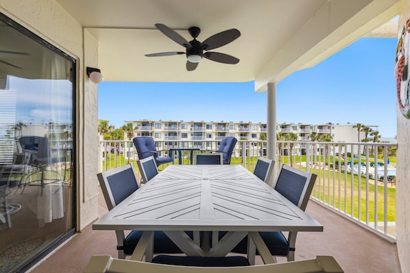 A balcony with a table and chairs, a ceiling fan, and a view of a residential building.