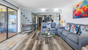 A living room with a glass coffee table, a sofa, and a colorful painting on the wall. - Picture Perfect at Colony Reef Club 1310 (St. Augustine)