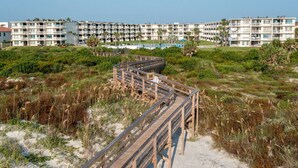 A wooden boardwalk leading to a beachfront area with a large hotel complex in the background. - Picture Perfect at Colony Reef Club 1310 (St. Augustine)