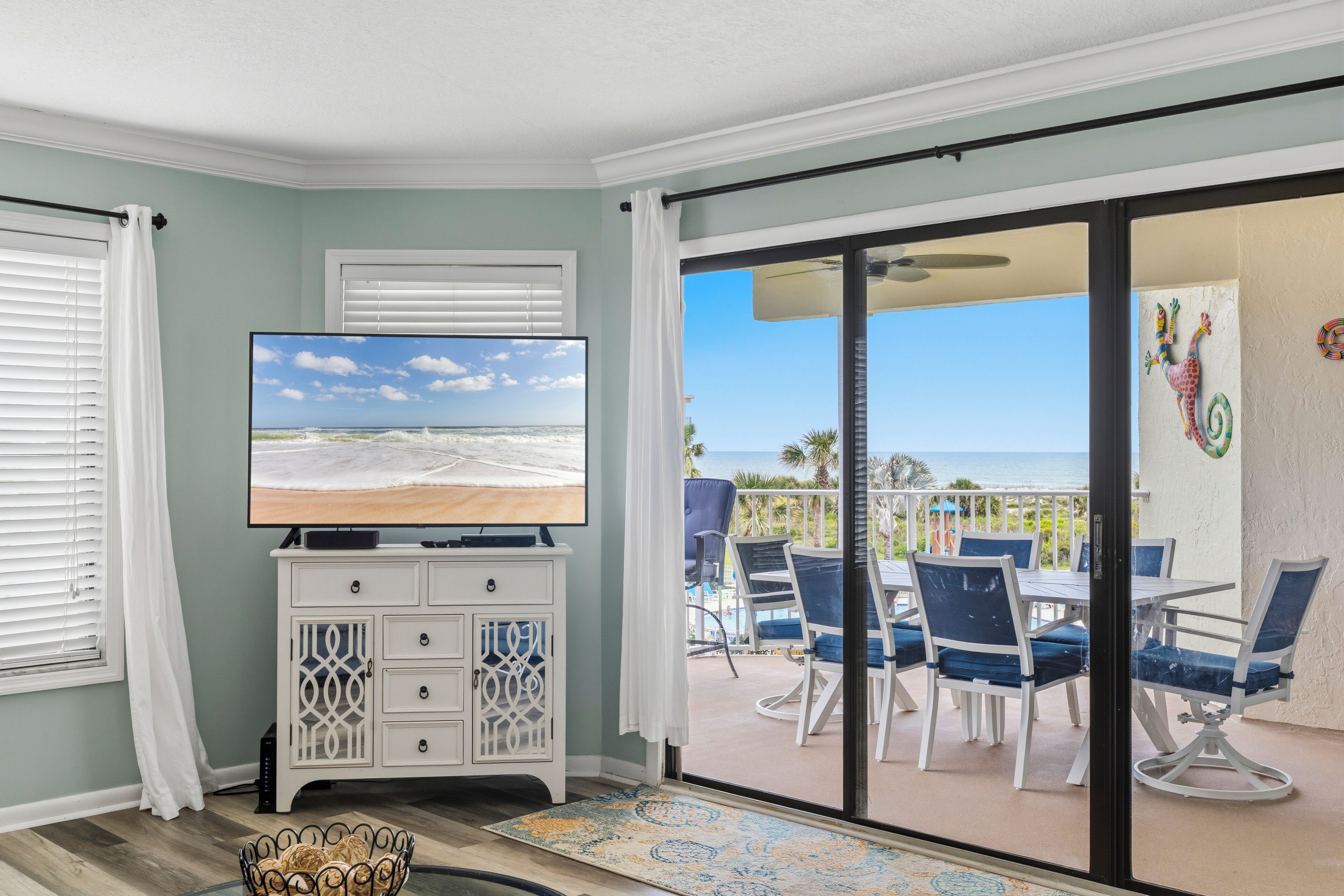 A room with a TV, a white cabinet, a patterned rug, and a balcony with chairs and a table.