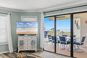 A room with a TV, a white cabinet, a patterned rug, and a balcony with chairs and a table.
