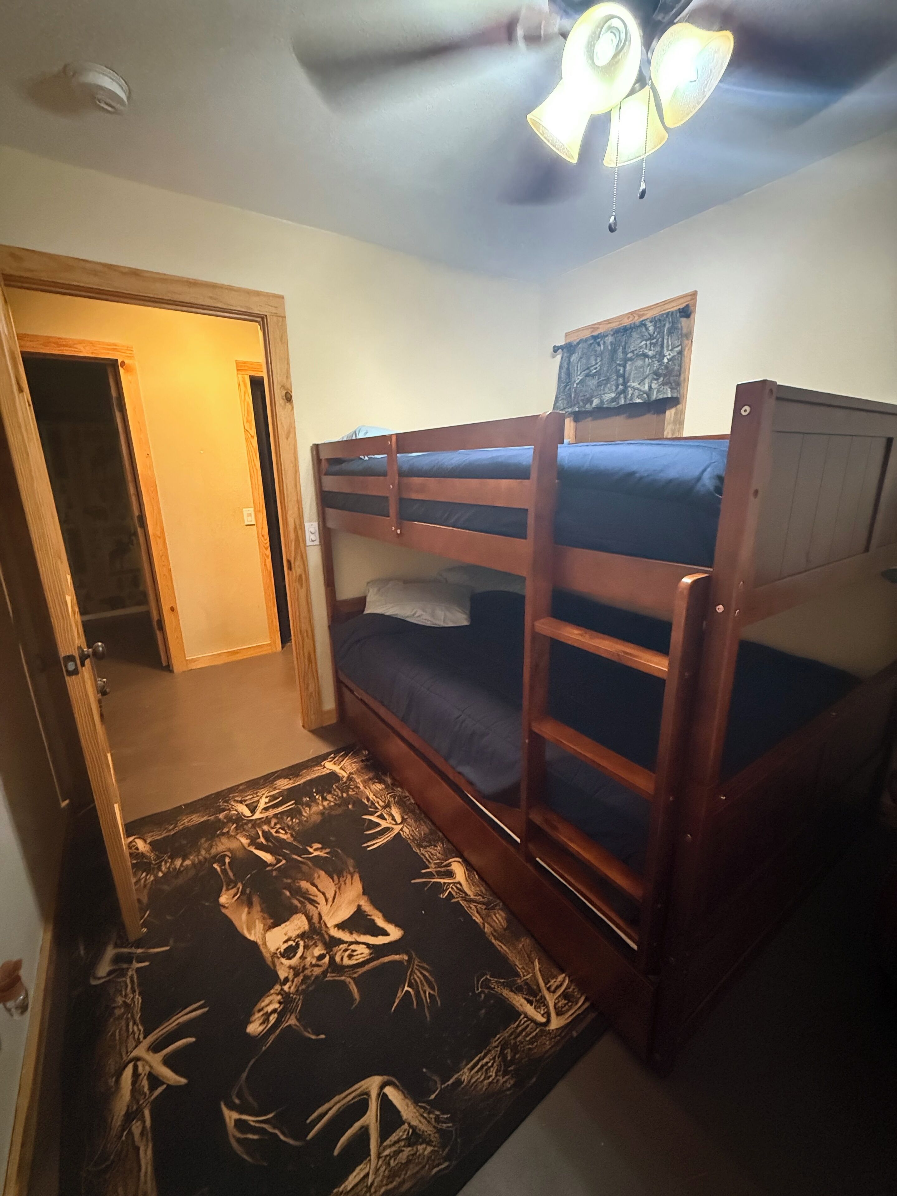 Une chambre avec un lit superposé, un ventilateur de plafond, une porte et un tapis à motifs.