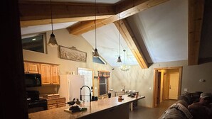 Eine geräumige Loft-Küche mit hohen Decken und freiliegenden Balken, eine große Kücheninsel mit Barbewirtung und eine gemütliche Sitzecke mit Sofa und Kissen.