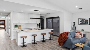 Una cocina moderna con armarios blancos, una isla central con taburetes y una puerta gris.