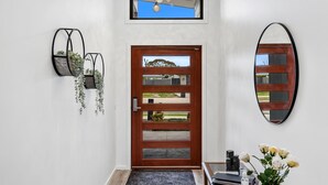 Un recibidor moderno con puerta de madera, espejo en la pared y una pequeña planta de interior.