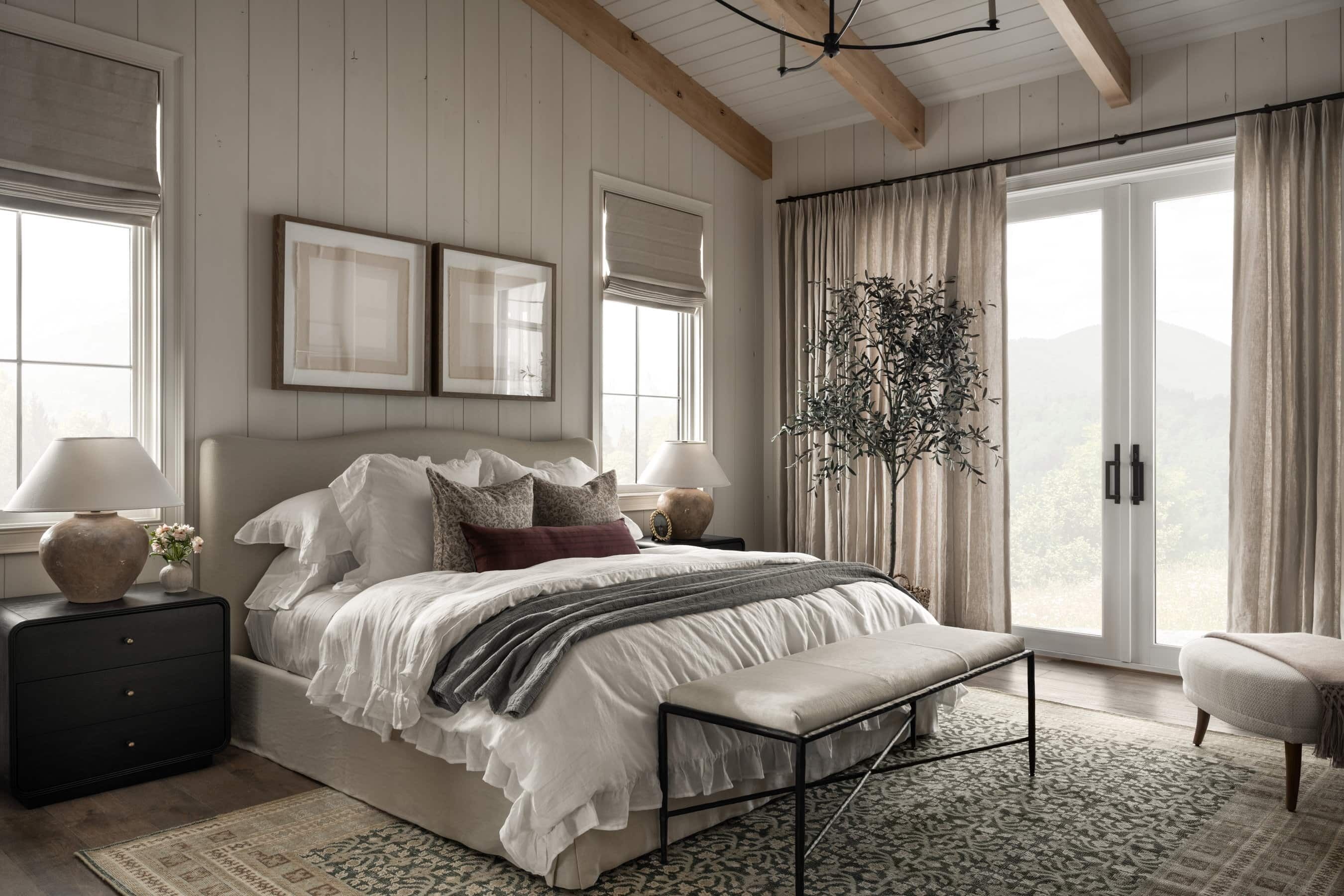 A bedroom with a large bed, bedside tables, a bench, and a view through a sliding glass door.