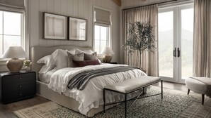 Une chambre à coucher avec un grand lit, des tables de chevet, un banc et une vue sur l’extérieur, accessible par une porte-fenêtre coulissante.