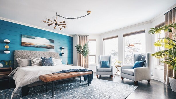 Une chambre à coucher avec un lit, deux fauteuils, un banc, un lustre et une grande fenêtre avec des rideaux.