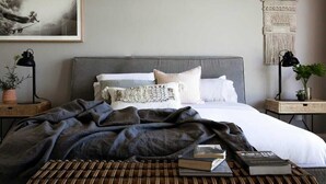 Une chambre à coucher avec un lit, une table de chevet avec une lampe, une décoration murale en macramé et un tableau encadré accroché au mur.