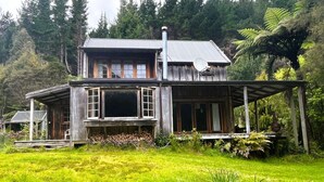 A rustic wooden house with a large front porch, surrounded by lush greenery and trees. - Private seaside cottage with boat only access. (Havelock)
