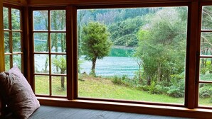 A room with a large bay window overlooking a lake and forest. - Private seaside cottage with boat only access. (Havelock)