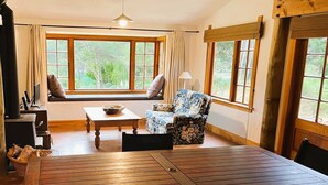 A cozy room with a large window, a wooden table, a sofa, and a chair. - Private seaside cottage with boat only access. (Havelock)