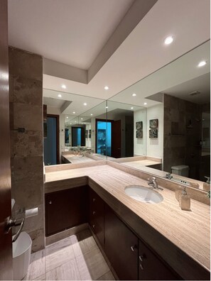 Une salle de bain moderne dotée d’un grand miroir, de deux vasques et d’une douche à l’italienne.