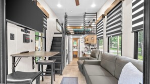 A compact RV interior with a kitchenette, a dining area, a sofa, and a staircase leading to an upper level. - “Special Place”Short Term Rentals Tiny Home Springville,Tennessee 148 (Springville)