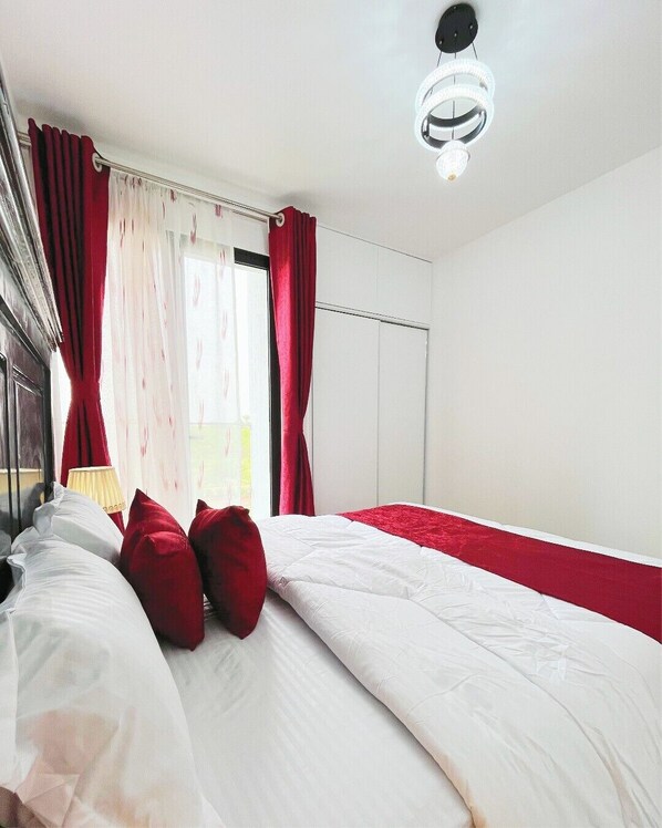 Un dormitorio con cama, cortinas rojas, una ventana y una lámpara de techo.