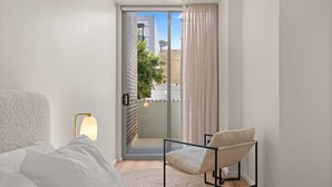Ein modernes Hotelzimmer mit einem Bett, einem Sessel, einer Lampe und einer Schiebetür, die auf einen Balkon führt.