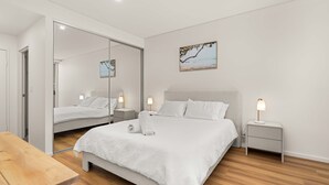 Ein modernes Schlafzimmer mit einem großen Bett, Nachttischen mit Lampen, einem Holzboden und einem Spiegel.