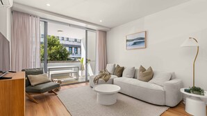 Ein modernes Wohnzimmer mit einer Couch, einem Couchtisch und einer Lampe. Ein Fenster mit Vorhängen, eine Pflanze und ein Gemälde sind an der Wand zu sehen.