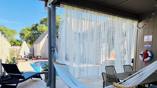 Een overdekt terras met een zwembad, tuinmeubilair en een hangmat.