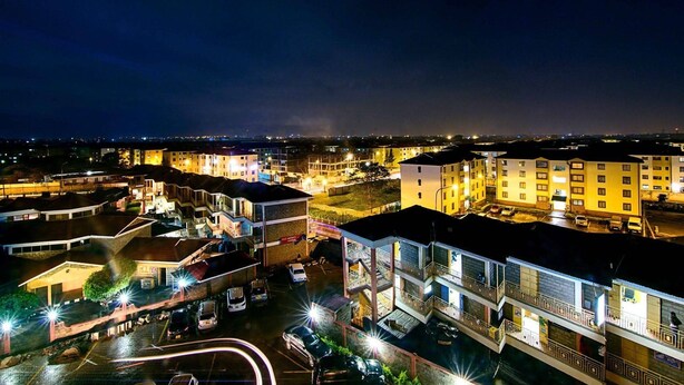 Un hotel de varios pisos con estacionamiento y vista de la ciudad iluminada de noche.
