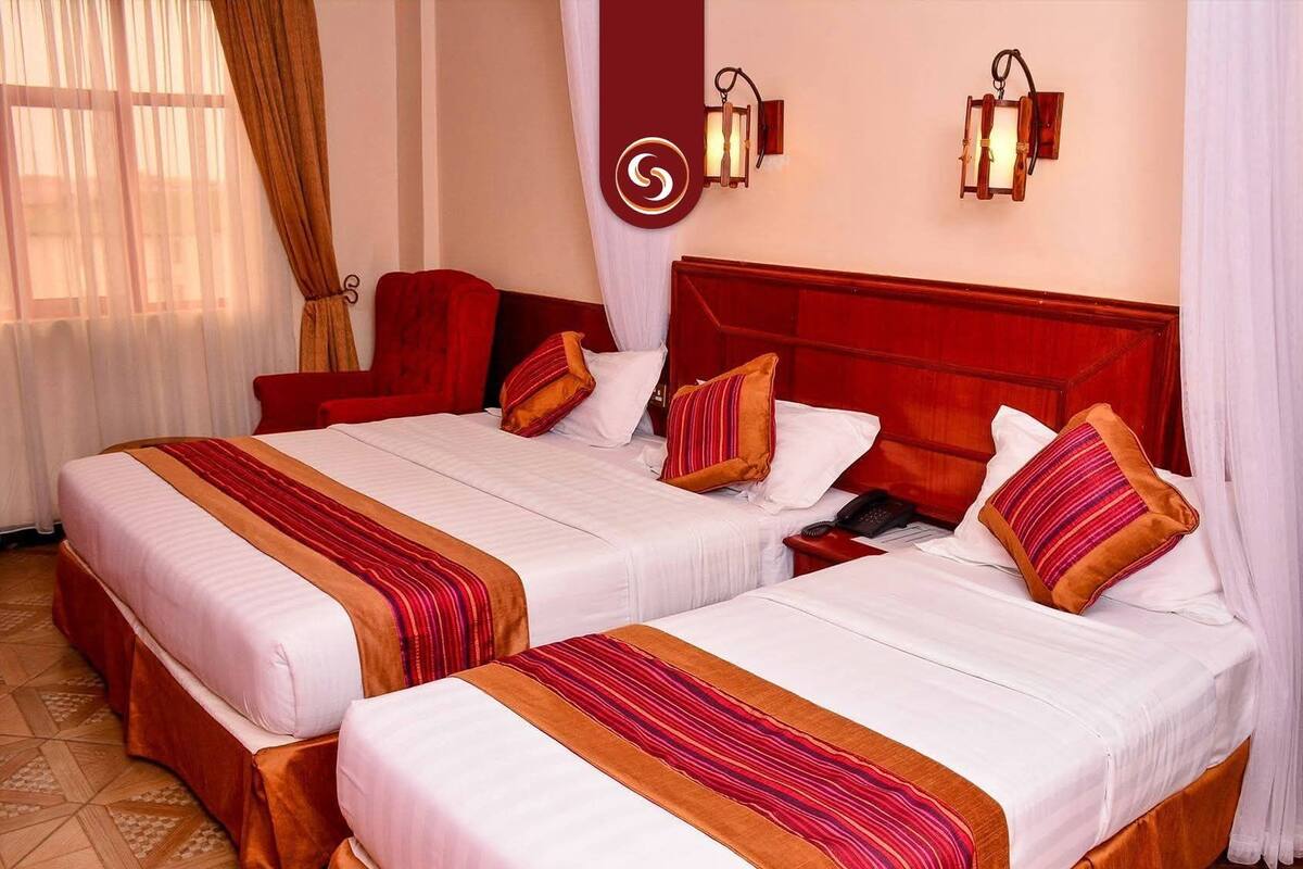 Ein Hotelzimmer mit zwei Betten, jeweils mit einer rot-weiß gestreiften Tagesdecke, einem Holz-Kopfteil und einem Nachttisch mit Telefon.