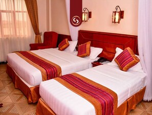 A hotel room with two beds, each with a red and white striped bedspread, a wooden headboard, and a nightstand with a telephone. - Seasons Airport Hotel Nairobi (Nairobi)