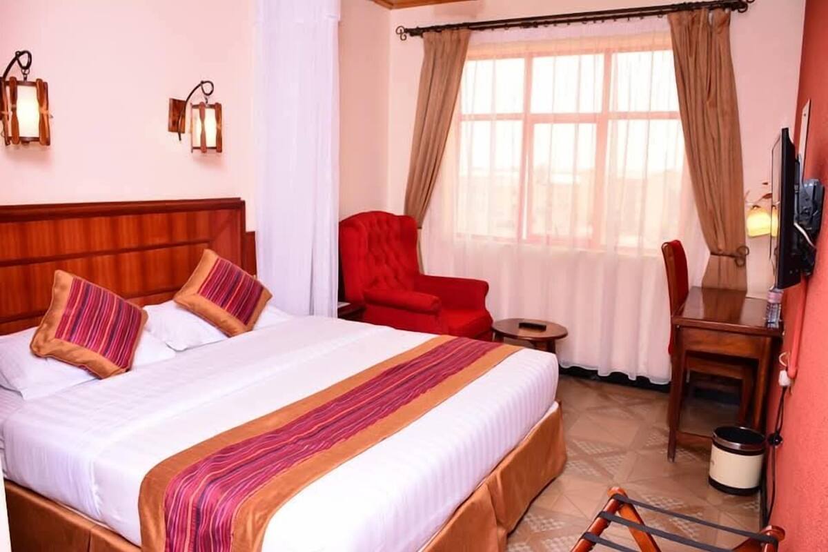 Ein Hotelzimmer mit einem großen Bett, einem roten Sessel, einem kleinen Tisch und einem Fernseher.