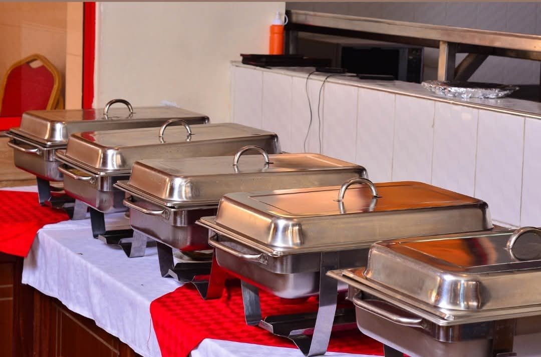 A buffet setup with multiple stainless steel chafing dishes on a table covered with a white tablecloth and red runners.