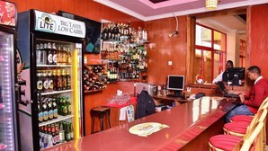 Un bar con mostrador, estanterías llenas de botellas y un refrigerador.
