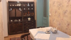 A dining area with a table set for two, a wooden cabinet with dishes, and a floral wallpapered wall. - 4-bedroom apartment in Karlovy vary (Karlovarský kraj)