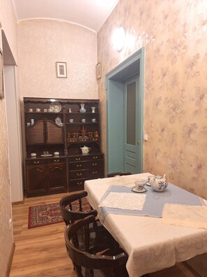 Uma área de refeições com uma mesa posta para dois, um armário de madeira com louças e uma parede revestida de papel de parede floral.