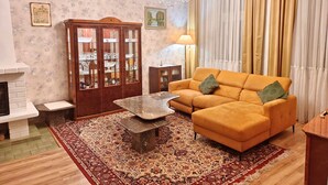 A living room with a sofa, a coffee table, a fireplace, a chandelier, and a large window with curtains. - 4-bedroom apartment in Karlovy vary (Karlovarský kraj)